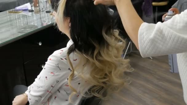 20 Eylül 2019 - Kamenskoye, Ukrayna: Profesyonel kuaför, güzellik stüdyosunda ombre tekniği ile boyalı uzun saçlı güzel bir genç kadın için saç spreyi ile saç stili yapıyor — Stok video
