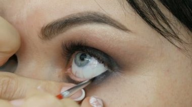 Profesyonel makyaj sanatçısı güzel genç bir kadının gözlerine makyaj uygular. Göz makyajı dumanlı gözler.