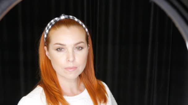Bella rossa dai capelli quarantenne donna luminosa con un cerchio di elastico sulla testa posa davanti alla telecamera in studio su sfondo nero — Video Stock