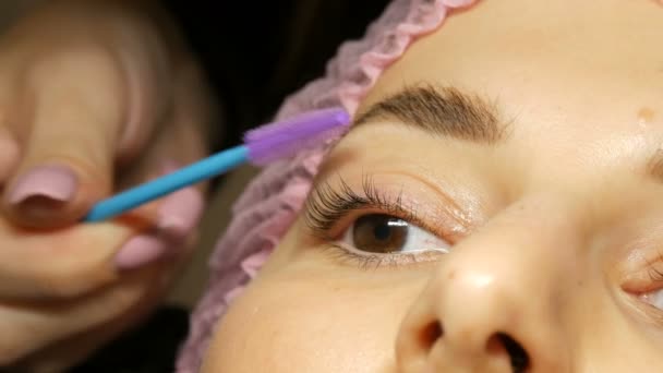 A special silicone brush comb combing long eyelashes to a client in beauty salon after lamination of eyelashes — Stockvideo