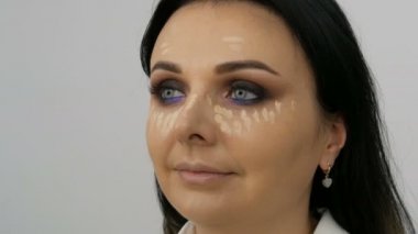 Makyaj sanatçısının yakın plan görüntüsü mavi gözlü güzel bir kadının yüzüne özel bir fırçayla fondöten kremi sürüyor.