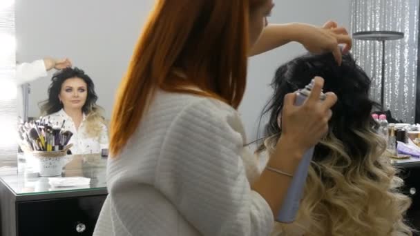 Setembro 20, 2019 - Kamenskoye, Ucrânia: cabeleireiro profissional estilista faz estilo de cabelo com laca para uma bela jovem com cabelo longo tingido com técnica ombre no estúdio de beleza — Vídeo de Stock