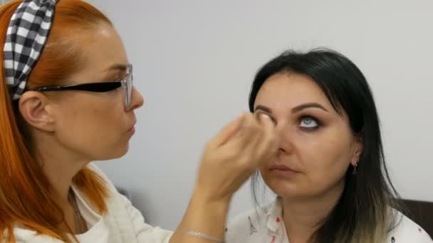 Profissional artista de maquiagem estilista aplica maquiagem aos olhos da bela jovem. Eyeliner maquiagem olhos fumegantes — Vídeo de Stock