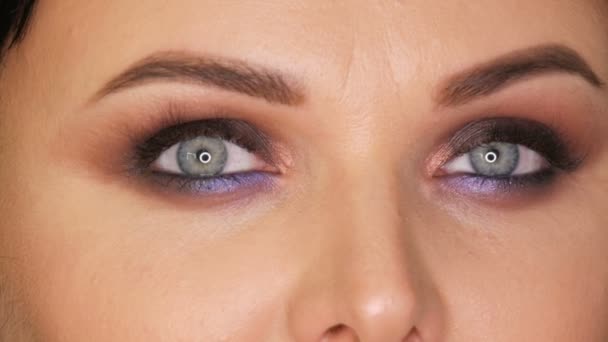 Mulher bonita nova com olhos azuis brilhantes e olhos fumegantes da maquilhagem da noite com sombra de olhos azul e roxo no fundo preto fechar — Vídeo de Stock