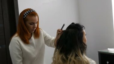 20 Eylül 2019 - Kamenskoye, Ukrayna: Profesyonel kuaför saç stilisti, güzellik stüdyosunda uzun saç teli tekniği olan güzel bir genç kadına özel tarak ve saç spreyi kullanıyor