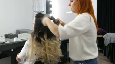 Profesyonel kuaför stilistliği, saç maşasıyla, güzellik stüdyosundaki ombre tekniğini kullanan uzun saçlı güzel bir kadına kıvırcık saç yapar.