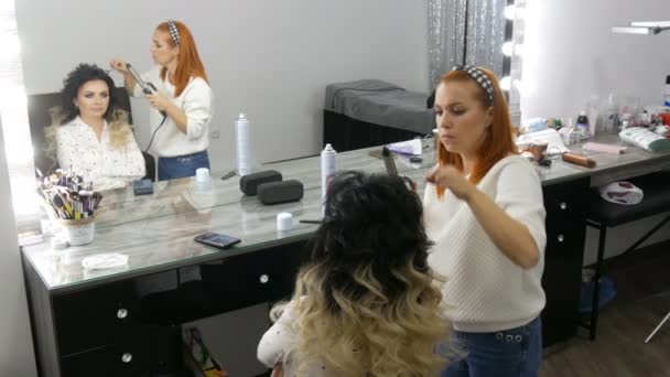 El peinado profesional hace rizos de rizos con la ayuda de una rizadora a una hermosa mujer joven con el pelo largo teñido utilizando la técnica ombre en el estudio de belleza — Vídeo de stock