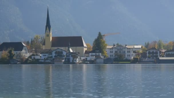 Schöne alte Kirche an lebendigem Ort vor dem Hintergrund der bayerischen Alpen am Ufer des Tegernsees — Stockvideo