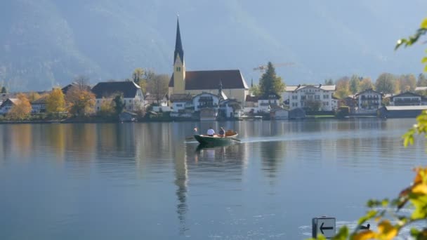 Un barquero transporta gente al otro lado, en el fondo de una hermosa y pintoresca iglesia en el lago Tegernsee, Baviera, Alemania — Vídeos de Stock