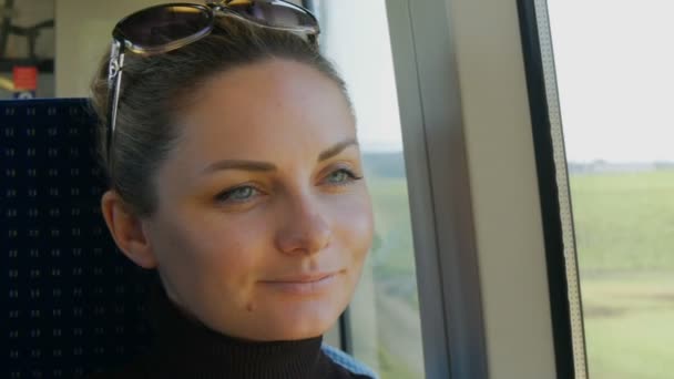 Retrato de una hermosa joven con ojos verdes y largas pestañas negras paseos en tren mirando soñadora y pensativamente por la ventana . — Vídeo de stock