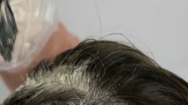 Özel fırça ile saçlarını kendini aidat orta yaşlı bir kadının büyümüş gri kökleri, yakın görünüyor. Beyaz bir arka planda bir kadınların kafası koyu saçlı ve beyaz kökleri. Saç Bakımı yakın görünüm