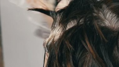 Özel fırça ile saçlarını kendi renklendiren orta yaşlı bir kadının büyümüş gri kökleri. Beyaz bir arka planda bir kadınların kafası koyu saçlı ve beyaz kökleri. Salon yakın görünüm saç bakımı.
