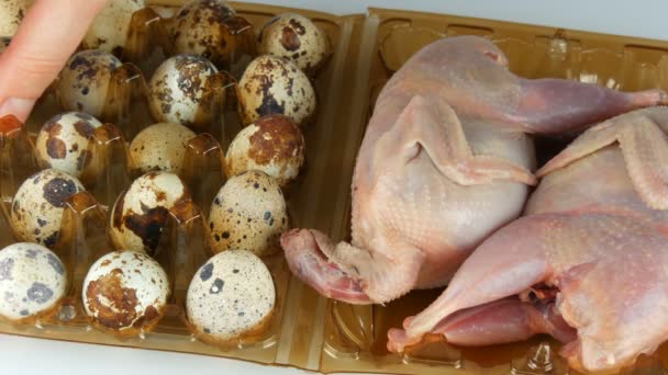 Carne fresca de codorniz en una bandeja de plástico marrón junto a los huevos de codorniz sobre un fondo blanco. Las manos femeninas toman los huevos en la bandeja . — Vídeo de stock