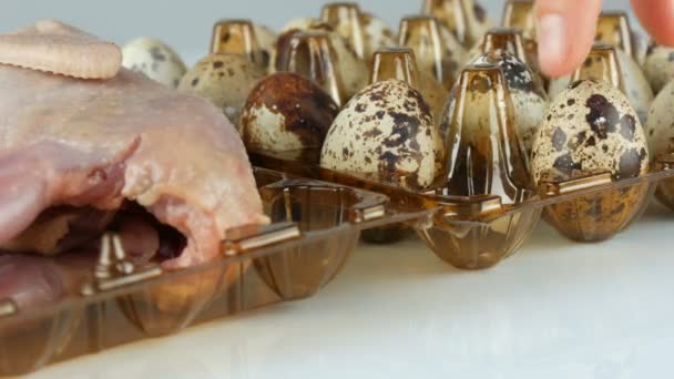 Čerstvé maso křepelek v plastovém hnědém tácu vedle křepelčích vajec na bílém pozadí — Stock video