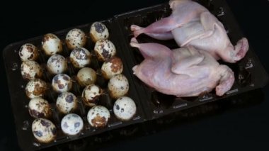 Siyah arka plandaki bıldırcın yumurtalarının yanında plastik kahverengi tepside taze bıldırcın eti.