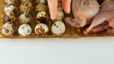 Beyaz arka planda bıldırcın yumurtalarının yanında plastik kahverengi tepside taze bıldırcın eti. Dişi eller yumurtaları alır ve tepsiye koyar..