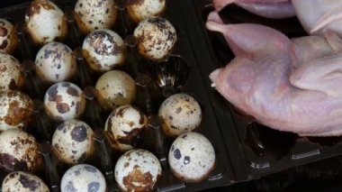 Siyah arka plandaki bıldırcın yumurtalarının yanında plastik kahverengi tepside taze bıldırcın eti.