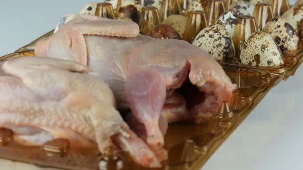 Свіже м'ясо перепелів у пластиковому коричневому лотку поруч з перепелиними яйцями на білому тлі обертаються — стокове відео