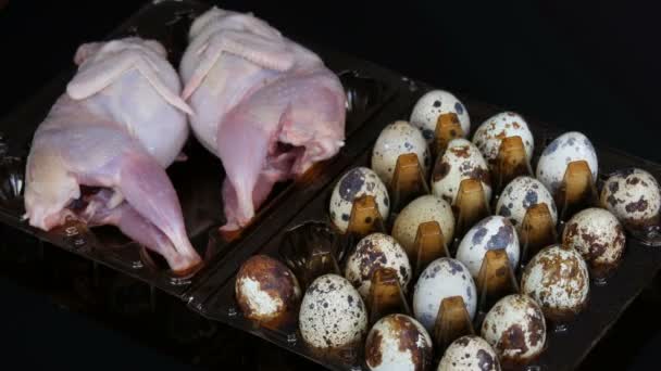 Carne fresca de codorniz en una bandeja de plástico marrón junto a los huevos de codorniz sobre un fondo negro. Las manos femeninas toman y ponen los huevos en la bandeja . — Vídeo de stock