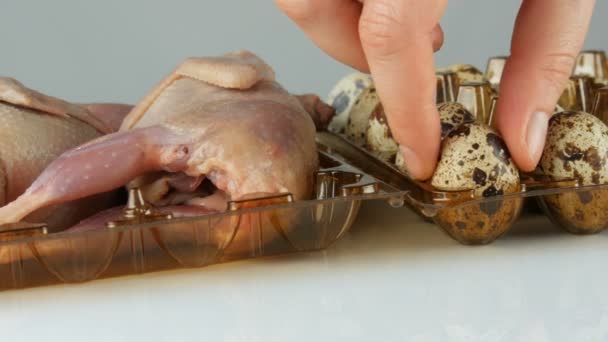 白い背景にウズラの卵の横にプラスチック製の茶色のトレイにウズラの新鮮な肉。女性の手はトレイに卵を入れて. — ストック動画