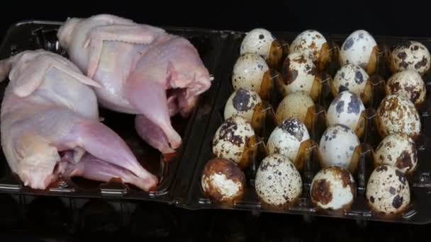 Свежее мясо перепела в пластиковом коричневом подносе рядом с перепелиными яйцами на черном фоне вращаются — стоковое видео