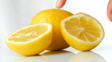 Beyaz arka planda taze, sulu sarı bir limon. Kadın eli olgun limonu alır