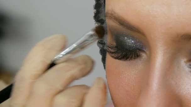 Makijaż artysta sprawia, że modele smoky oczy za pomocą specjalnej szczotki szare Eyeshadow, oczy i rzęsy dziewczyny bliska. Profesjonalna wysoka moda. — Wideo stockowe