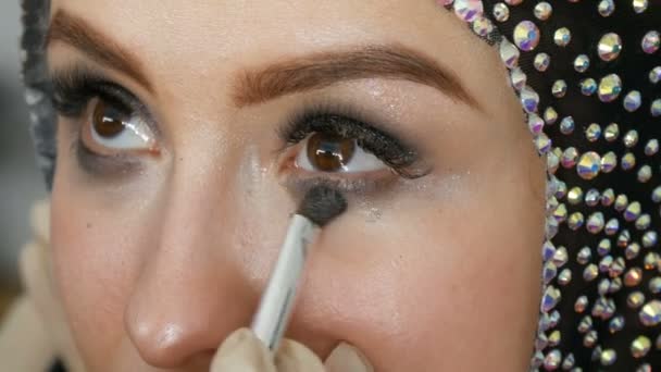 Maquillaje artista hace modelos ojos ahumados con la ayuda de un cepillo especial sombra de ojos gris, ojos y pestañas de niña vista de cerca. Profesional de alta moda . — Vídeo de stock