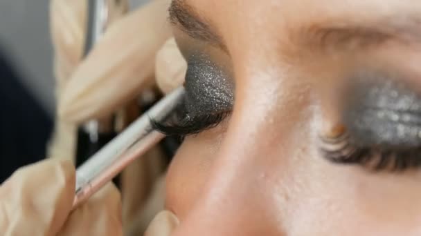 Make-up-Artist macht Models rauchige Augen mit Hilfe spezieller Pinsel grauen Lidschatten, Augen und Wimpern von Mädchen Nahsicht. professionelle Mode. — Stockvideo
