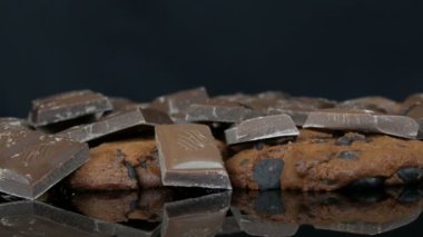 Çikolatalı kurabiyeler ve siyah arka planda çikolata parçaları ve ayna yüzeyi.