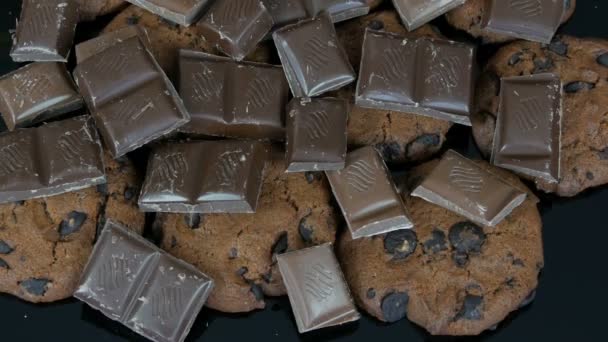 Biscoitos de chocolate e pedaços de chocolate no fundo preto elegante e uma superfície de espelho — Vídeo de Stock