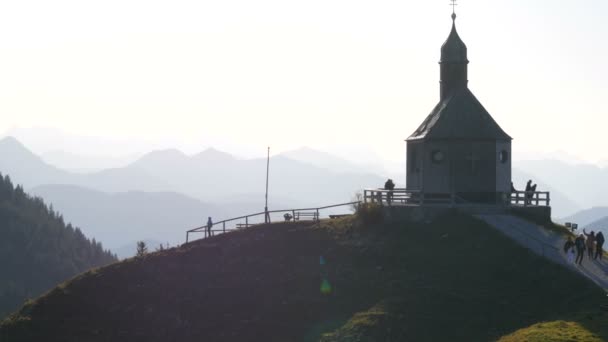 Tegernsee, Tyskland - 23 oktober 2019: Gamla kyrkan på den vackra pittoreska sluttningen av bayerska Alperna nära vilken turister promenera — Stockvideo