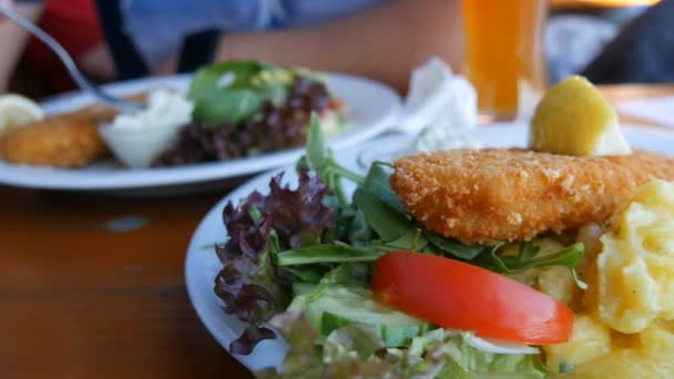 아름답게 요리된 생선의 두 부분은 고급 레스토랑의 흰 접시 위에서 반죽을 하고 있습니다. 미국 바이에른주 감자 샐러드와 레몬이 들어 있는 야채 근처 — 비디오