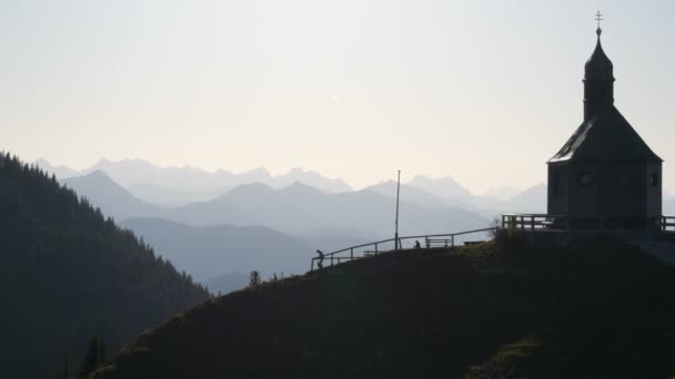 德国泰格纳什- 2019年10月23日：位于巴伐利亚阿尔卑斯山美丽风景如画的斜坡上的一座古老教堂，游客们在此漫步 — 图库视频影像