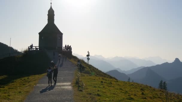Tegernsee, Alemania - 23 de octubre de 2019: Iglesia antigua en la hermosa ladera pintoresca de los Alpes bávaros cerca de la cual pasean los turistas — Vídeo de stock