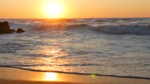 日の出や海岸では非常に美しい夕日。砂浜と波がビーチで打ちます。泡の大きな嵐の波 — ストック動画