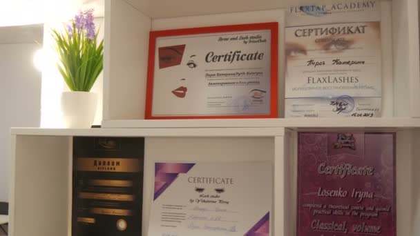 Kamenskoye, Ukrayna - 11 Kasım 2019: Pek çok farklı lashmaker diploması ve sertifikası şık bir güzellik salonunda raflarda. Rusça ve İngilizce yazılar. — Stok video