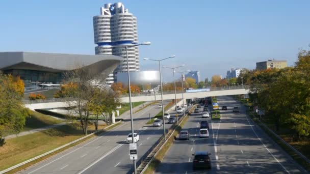 München, Duitsland - 25 oktober 2019: Hoofdkantoor van Bmw in München. De toren wordt vaak genoemd als een van de meest opvallende voorbeelden van architectuur in München. Auto 's die over de weg passeren — Stockvideo