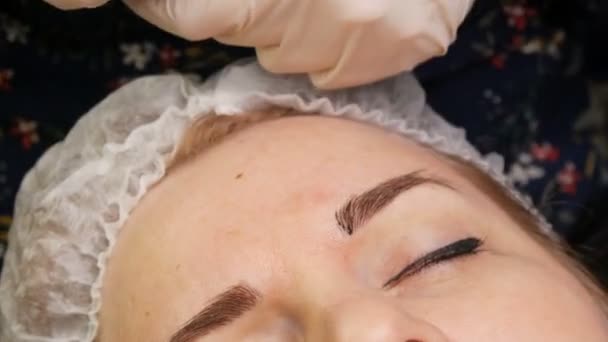 En kosmetolog i handskar, med en speciell nål, applicerar ett färgpigment under huden på ögonbrynen. Korrigering av ögonbrynsform med hjälp av hårmikroblödning, permanent make-up, ögonbrynstatuering — Stockvideo