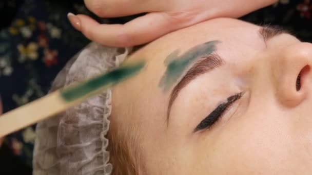 Corrección de cera de la forma de las cejas. esteticista aplica cera verde cálido en las cejas y elimina el exceso de cabello con tira especial . — Vídeos de Stock