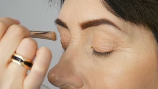 Maquillaje artista hacer maquillaje de ojos a la mujer de mediana edad con ojos azules. Maquillaje de edad. Retrato de cerca. Aplicar polvo con pincel — Vídeos de Stock