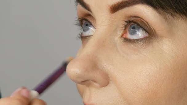 Maquillaje artista hacer maquillaje de ojos a la mujer de mediana edad con ojos azules. Maquillaje de edad. Retrato de cerca. Aplicar polvo con pincel — Vídeos de Stock