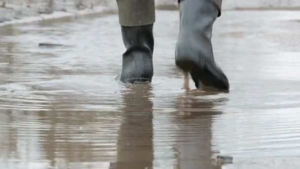 Een man loopt door de modderige plas in rubber laarzen. — Stockvideo