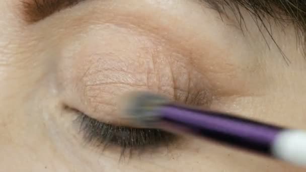 예술가는 파란 눈을 가진 중년의 여성에게 눈 화장을 한다. 연령 구성. 확대 사진. 붓으로 분말을 친다 — 비디오