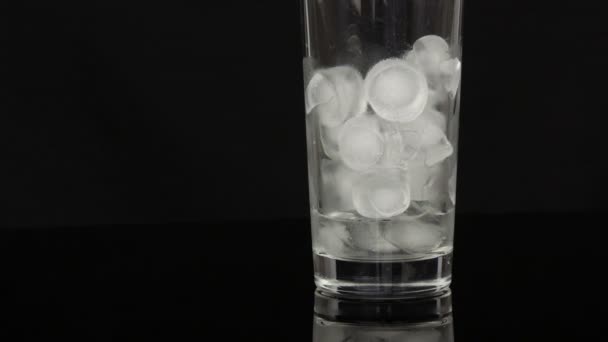 Prázdný dlouhý skleněný pohár s ledem na černém pozadí. — Stock video