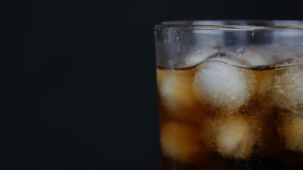 Bolle di cola fredda in un bicchiere lungo trasparente con ghiaccio su fondo nero vista da vicino . — Video Stock