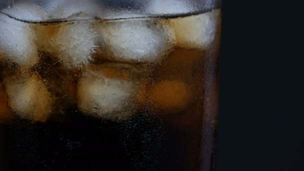 Bubblor av kall Cola i ett genomskinligt långt glas med is på en svart bakgrund närbild. — Stockvideo