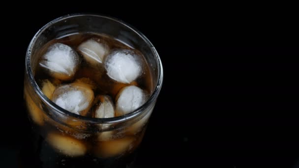 Bubbels van koude Cola in een transparant lang glas met ijs op een zwarte achtergrond close-up te bekijken. — Stockvideo