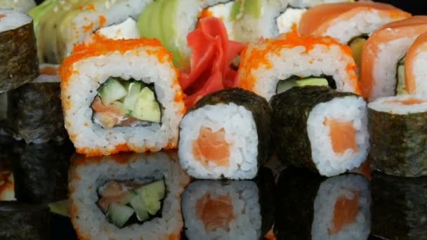 Una variedad de juegos de rollos de sushi de colores y jengibre rotan en la superficie del espejo sobre un fondo negro. Cocina japonesa en estudio — Vídeo de stock