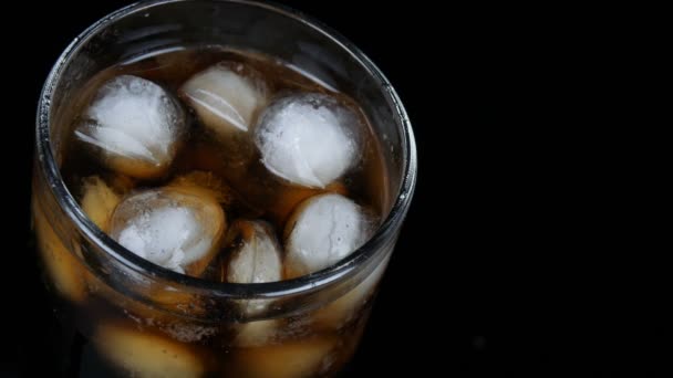 Bubbels van koude Cola in een transparant lang glas met ijs op een zwarte achtergrond close-up te bekijken. — Stockvideo